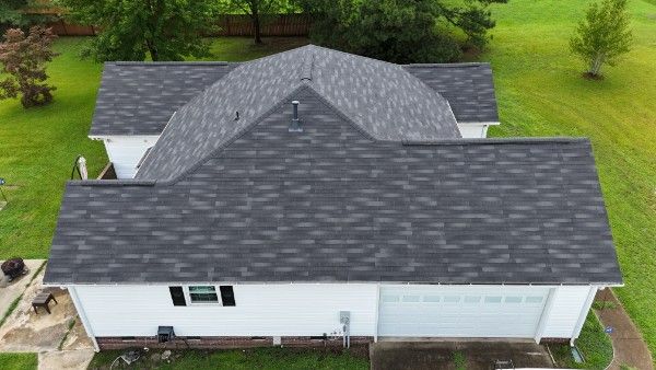 Overhead view of a house with gray architectural asphalt shingles and white vinyl siding surrounded by a lawn.