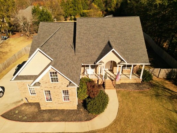 Aerial view of a brick house with gray architectural asphalt shingle roofing and a covered front porch.