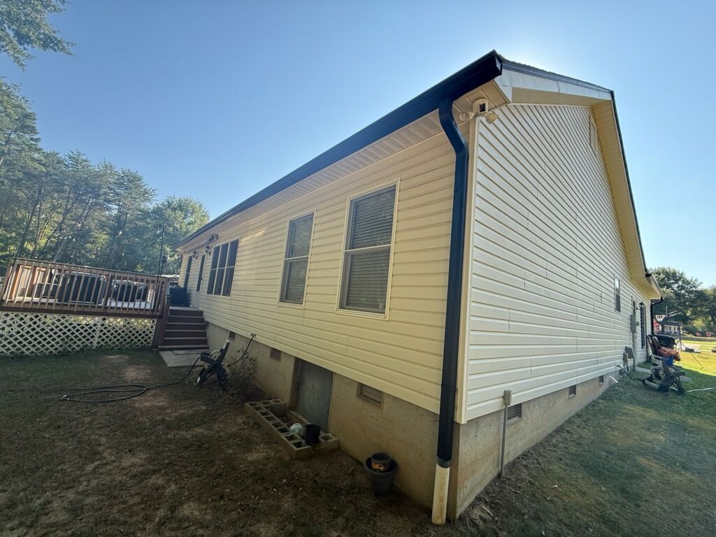 Rear view of a house with yellow vinyl siding, black gutters and downspouts, and a wooden deck.